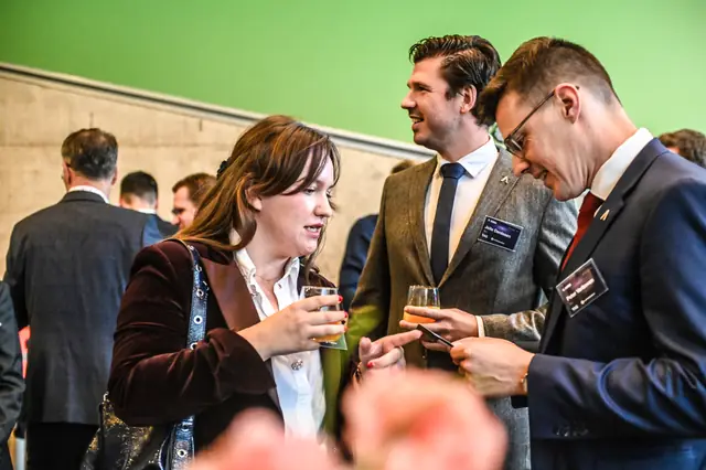 Three guests in conversation over a glass in the foyer.