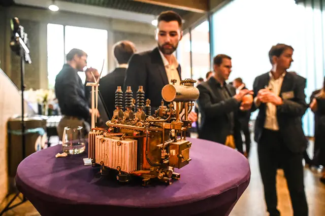 A copper scale model on a high table, with guests talking behind it.