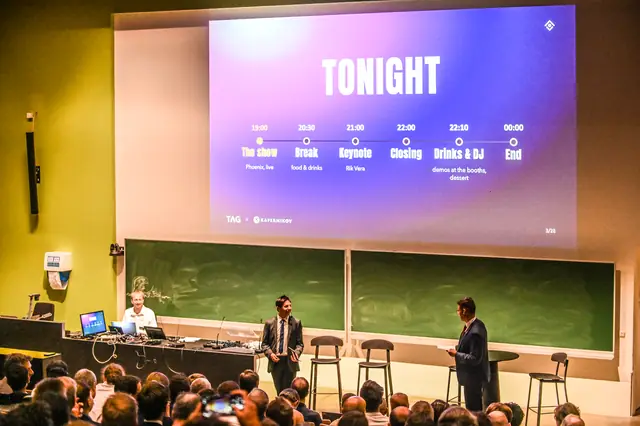 The aula seen from the back, with the running order of the evening on screen.