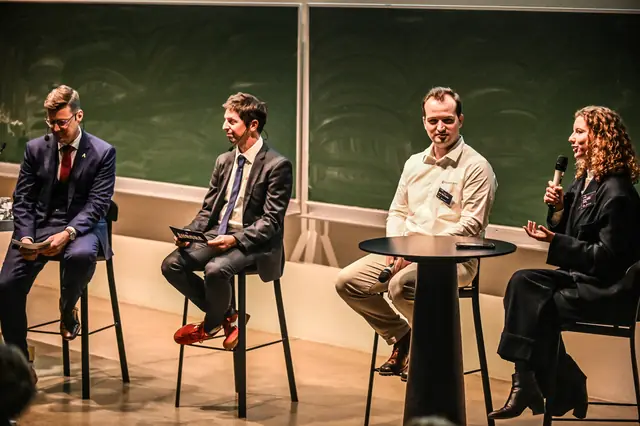 Four people on stools on stage during the walkthrough.