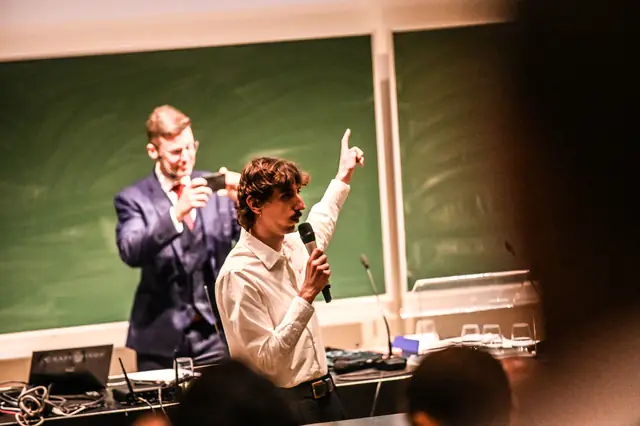 A speaker pointing upward, microphone in hand.