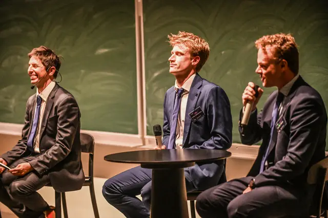 Three speakers sharing a laugh on stage.