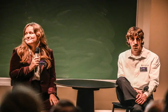 A speaker smiling at the audience, microphone in hand.