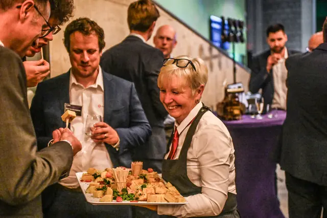 A smiling waitress offering a tray of bites.