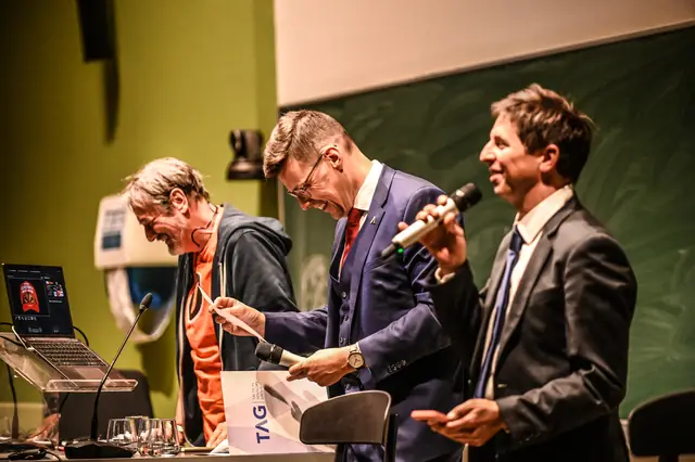 Rik Vera on stage with a TAG bag, next to two speakers with microphones.